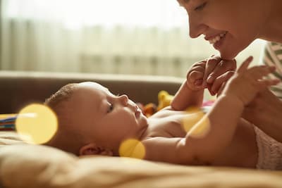 mother smiling at her baby and holding their hand